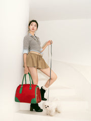 woman-standing-on-beige-stairs-back-against-wall-left-hand-holding-dog-leash-right-hand-carrying-red-boston-pet-bag